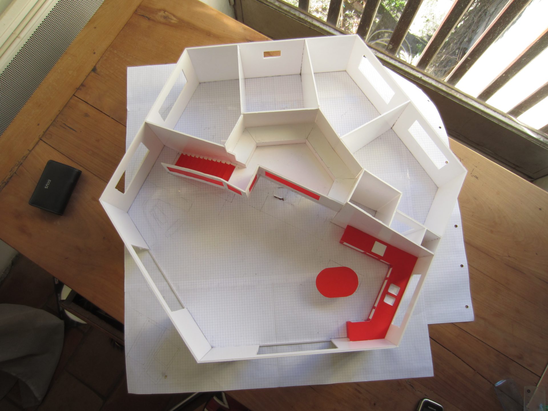 Maquette en carton blanc d'une maison de plain-pied, vue de dessus, toiture retirée. Les cloisons et le mobilier sont en rouge.